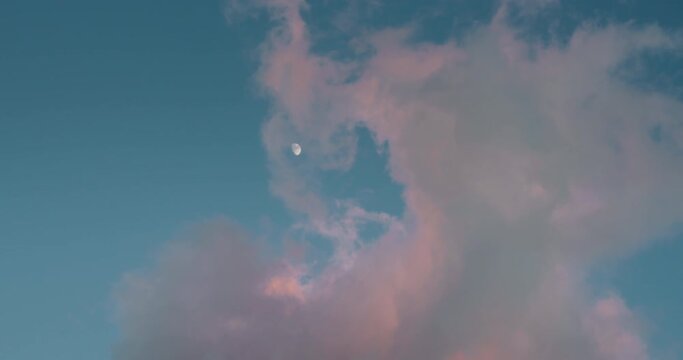 Waning gibbous moon on blue sunset sky with pink clouds.
