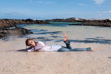 Wet young woman in clothes on the seashore in spring or summer under a blue sky