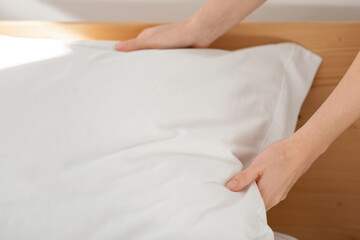Hands of caucasian millennial female puts soft white pillow on comfortable bed, makes bed