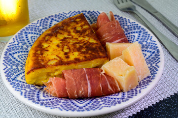 Spanish food, portion of potato omelette tortilla de patatas with onion served with cheese and jamon