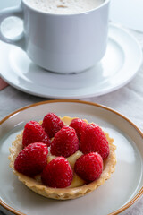 Breakfast with cup of black coffe and baked small tart with cream and fresh ripe red raspberry fruits