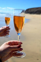 Beach party, hands with glass of rose champagne or cava sparkling wine, view on white sandy tropical beach and blue ocean water, romantic vacation, winter sun on Fuerteventura, Canary, Spain