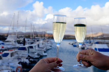 Obraz premium Everyday party, hands with glasses of cava or champagne sparkling wine in yacht harbour of Caleta Fuste, Fuerteventura, Canary islands vacation, Spain