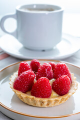 Breakfast with cup of black coffe and baked small tart with cream and fresh ripe red raspberry fruits