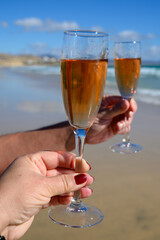Beach party, hands with glass of rose champagne or cava sparkling wine, view on white sandy tropical beach and blue ocean water, romantic vacation, winter sun on Fuerteventura, Canary, Spain