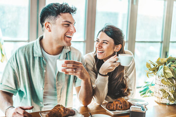 Happy couple enjoying breakfast drinking coffee at bar cafeteria - Lifestyle concept with guy and girl in love having date moment sitting at restaurant in the city centre - obrazy, fototapety, plakaty