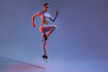 Fototapeta na wymiar Athletic active woman jumping on studio background with colored filter. Dynamic movement