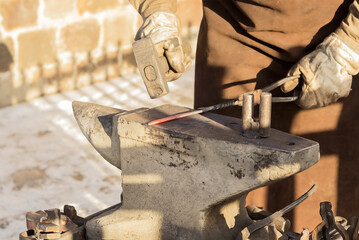 In the hand of a blacksmith, a working hammer for working on an anvil with a red-hot iron rod,...