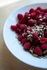 fresh red healthy raspberry with sunflower seed in white plate, wood background