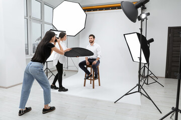 Professional photographer and assistant working with handsome model in modern photo studio