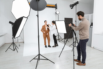 Professional photographer and stylist working with beautiful model in modern photo studio