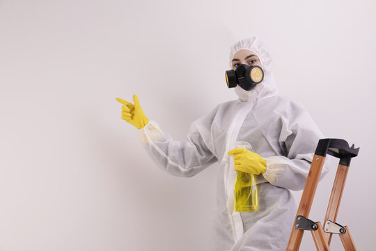 Woman In Protective Suit Cleaning Mold With Sprayer On Wall