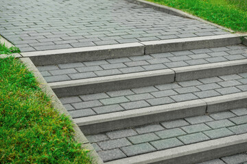 View of sidewalk steps and fresh green grass on sunny day. Footpath covering