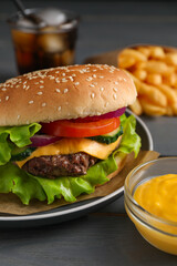 Delicious burger, soda drink and french fries served on grey wooden table, closeup