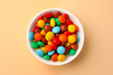 Bowl with tasty colorful candies on beige background, top view