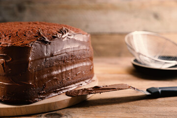 Delicious homemade layer cake with chocolate cream on wooden table, closeup