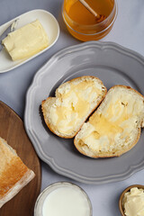 Sandwiches with butter, honey and milk on light grey table, flat lay