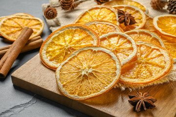 Many dry orange slices and spices on black textured table, closeup