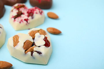 Tasty chocolate heart shaped candies with nuts on light blue background, closeup. Space for text