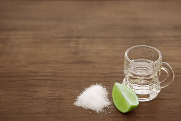 Mexican tequila shot with lime slice and salt on wooden table, space for text. Drink made from agave