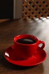 Red cup with aromatic coffee on wooden table indoors, closeup