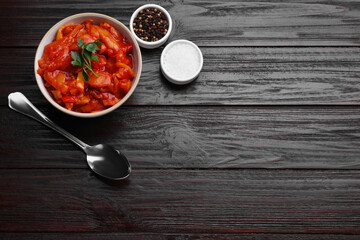 Delicious lecho and spices on black wooden table, flat lay. Space for text
