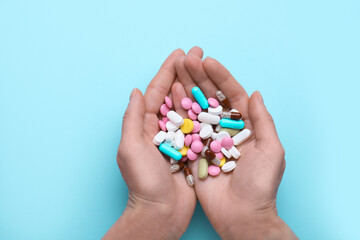 Woman holding colorful antidepressants on light blue background, top view