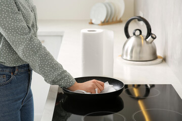 Woman wiping frying pan with paper towel in kitchen, closeup