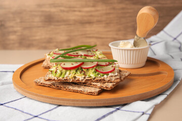 Fresh crunchy crispbreads with cream cheese, radish and green onion on beige table