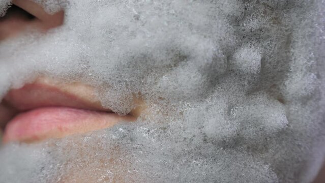A woman's face with a gray bubble clay mask in a close-up. A girl applies a nourishing charcoal mask to reduce wrinkles.
