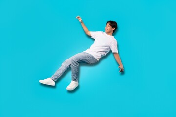 Asian Teenager Boy Falling In Mid Air Over Blue Background