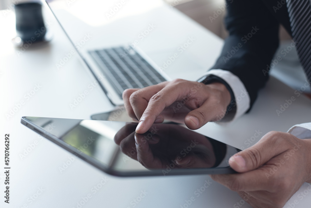 Wall mural Business man in black suit using digital tablet on desk at office. Businessman finger touching on blank screen tablet, online working with laptop computer on office table, close up