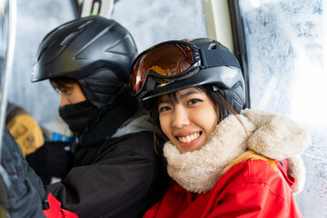 Asian couple rises to snowy mountain peak on cableway cabin practicing snowboard and ski at ski...