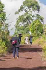  Travelers walking up a dirt road, with an exhausted gentleman stopping to catch his breath in front of this sloping road bamendjou, bafoussam, Cameroon