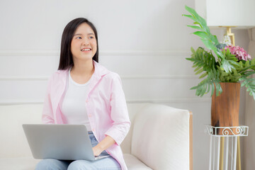 Young asian business woman work from home with laptop computer online to internet on sofa in living room, freelance girl using notebook sitting on couch with comfort and relax, lifestyles concept.