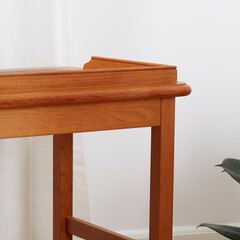 Vintage leather top writing desk, interior view in front of a luxurious curtain with houseplants. Close-up detail of wood lip on the desk surface.