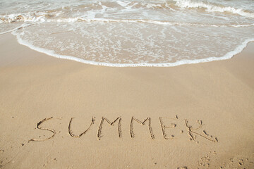 Summer 2023 lettering on the beach with wave and clear blue sea. 