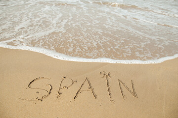 Spain lettering on the beach with wave and clear blue sea. 
