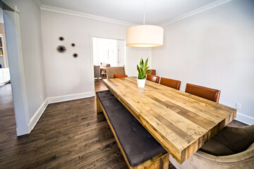 A modern dining room with a stained with a stained wood table, bench seating and upholstered chairs with a hanging drum light fixture