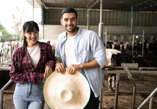 Portrait Of Couple Multi Racial Diversity  Asian And Hispanic Farmers Who Are Standing At The Cow Farm.