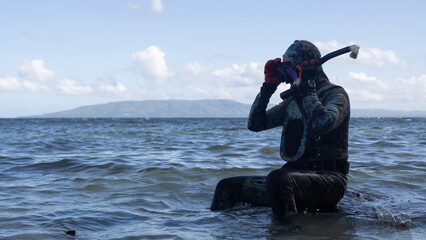a man in a wetsuit, with camouflage coloring, is preparing for spearfishing, with an underwater...