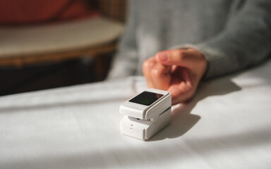 Closeup image of a woman using digital fingertip pulse oximeter device to measure oxygen and blood pulse rate