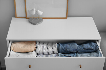 Open drawer with folded clothes in room, closeup