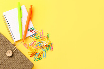Notebooks, pens and paper clips on yellow background