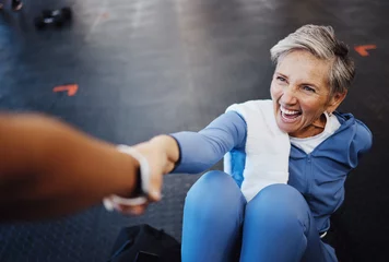  Senior woman, fitness and personal trainer with support and happy workout, exercise and muscle health on gym floor. Helping hand, coaching and elderly person with training sports for retirement care © Siphosethu F/peopleimages.com
