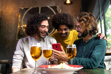 Young man showing to male friends mobile phone while having drinks together in pub.