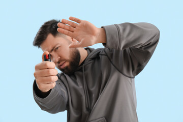 Young man with pepper spray for self-defence on blue background, closeup