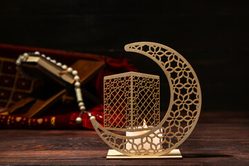 Decorative crescent with burning candle for Ramadan on dark wooden table, closeup