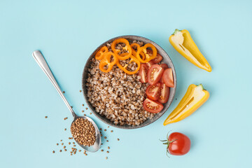 Bowl of tasty buckwheat porridge with fresh vegetables on blue background