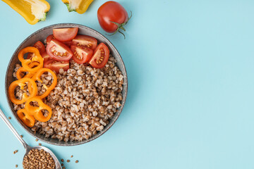 Bowl of tasty buckwheat porridge with fresh vegetables on blue background